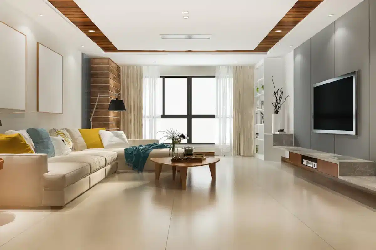 Modern living room interior featuring a white sectional sofa with yellow and blue cushions, a wooden coffee table, and a flat-screen TV on a grey wall