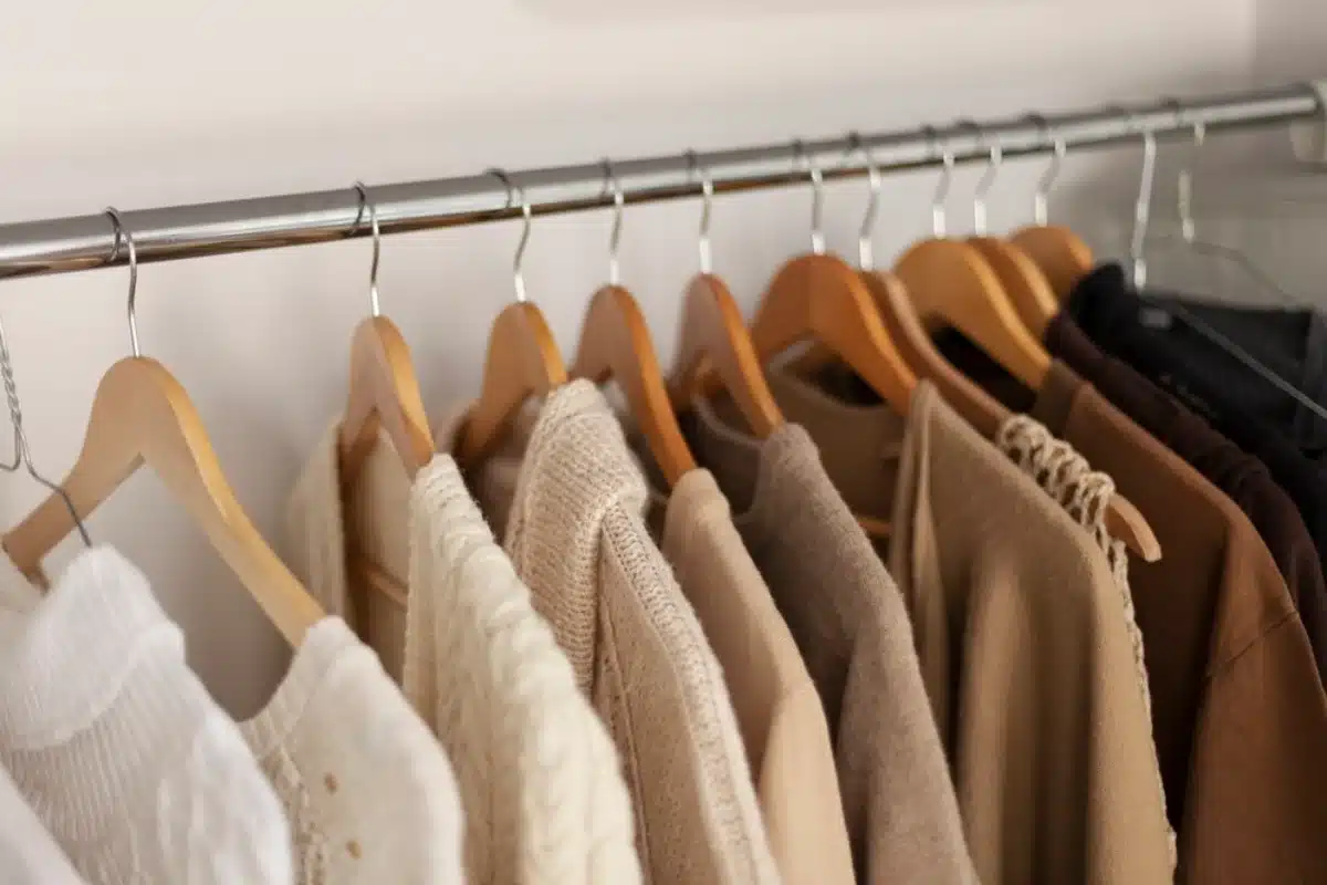 A row of neatly arranged clothes hanging on wooden and wire hangers on a metal rail.